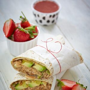 Zwei eingepackte Wraps liegen mit einer Schale Erdbeeren daneben auf einem Tablett.