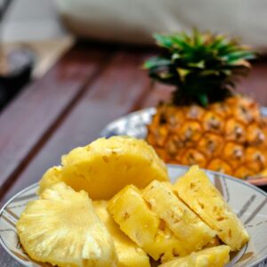 Eine Schale mit geschnittener Ananas und einer Ananasfrucht im Hintergrund.