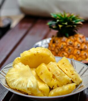 Eine Schale mit geschnittener Ananas und einer Ananasfrucht im Hintergrund.