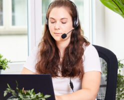 Junge Frau mit einem Headset sitzt vor ihrem Laptop im Gespräch.