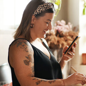 Eine junge Plus size Frau schaut auf ihr Smartphone, während sie am kochen ist.