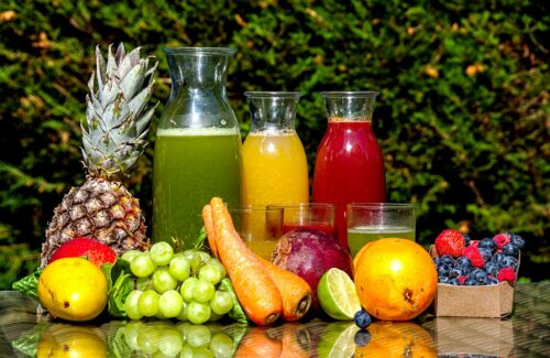 Frisches Obst und Gemüse und drei Karaffen mit frischem Saft und Gläsern sind auf einem Gartentisch drapiert.