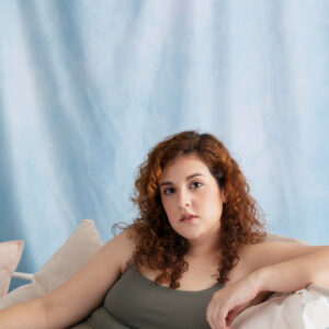 Eine junge plus size Frau sitzt im Sport set auf einem hellen Sofa.