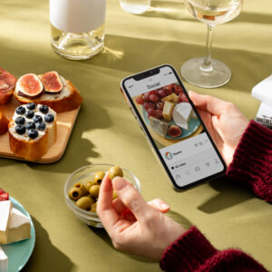 Ein Ausschnitt eines gedeckten Tisches und zwei Händen die ein Smartphone in der Hand halten.