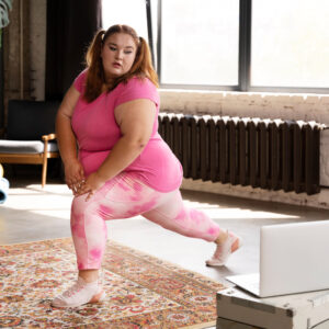 Eine junge plus size Frau macht long squats und schaut dabei auf ihren Laptop.