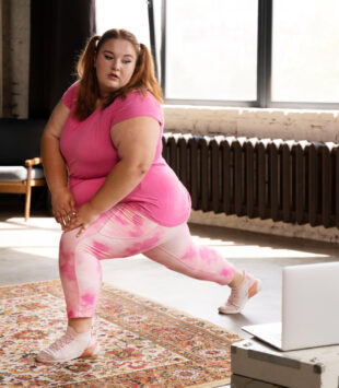 Eine junge plus size Frau macht long squats und schaut dabei auf ihren Laptop.