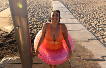Eine plus size Frau im Badeanzug hat einen Schwimmreifen um die Hüften und lächelt fröhlich.