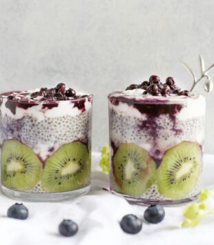 Zwei Gläser gefüllt mit Chiapudding, Kiwi und Beeren.