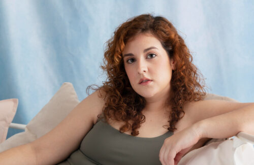 Eine junge Frau im Top sitzt auf einem Sofa und lehnt mit ihrem Arm auf der Lehne.