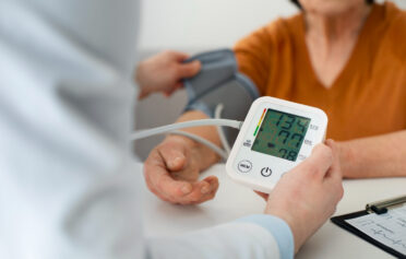 Ein Bildausschnitt, auf dem zusehen ist, wie eine medizinische Fachperson einer anderen den Blutdruck, mithilfe eines Blutdruckmessgerätes, misst.