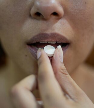 Eine Nahaufnahme eines Frauenmundes, der gerade eine Tablette in den Mund nimmt.