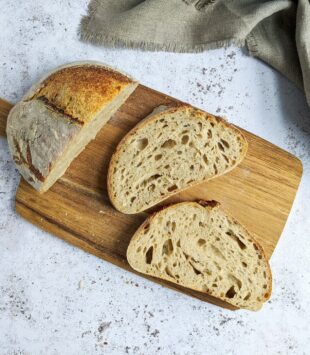 Eine Brett mit einem aufgeschnittenem Sauerteigbrot und zwei Scheiben daneben.