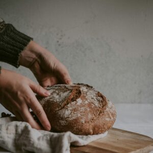 Zwei Hände nehmen einen Leib Brot von einem Holzschneidebrett.
