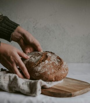 Zwei Hände nehmen einen Leib Brot von einem Holzschneidebrett.