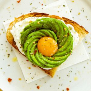 Eine halbe Scheibe Brot mit Avocado Streifen und einem Eigelb.