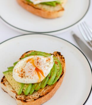 Ein Teller mit einer Scheibe Brot, die belegt ist mit Avocado und einem pochiertem Ei.