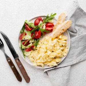 Ein Teller mit Rührei, frischem Gemüse und einer Scheibe Brot dazu.