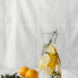 Eine große Glaskaraffe mit Wasser, Zitronenscheiben und frischen Kräuterzweigen.