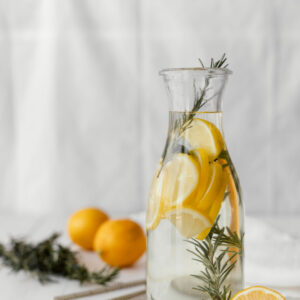 Eine große Glaskaraffe mit Wasser, Zitronenscheiben und frischen Kräuterzweigen.