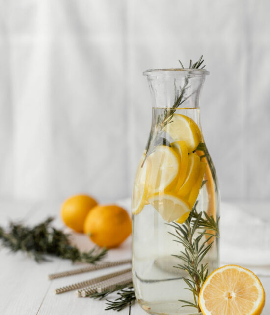 Eine große Glaskaraffe mit Wasser, Zitronenscheiben und frischen Kräuterzweigen.