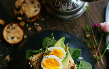 Ein Avocado-Spinat-Ei-Brot auf einem dunklen Keramik Teller.