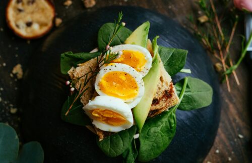 Ein Avocado-Spinat-Ei-Brot auf einem dunklen Keramik Teller.