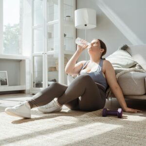 Frau sitzt auf dem Boden in Sportklamotten und trinkt wasser