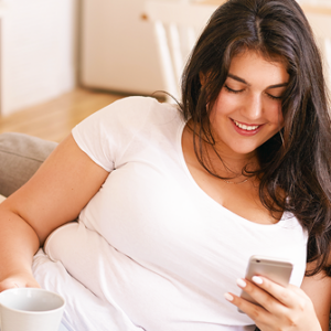 Lächelnde Frau liegt auf dem Sofa und schaut auf ihr Handy