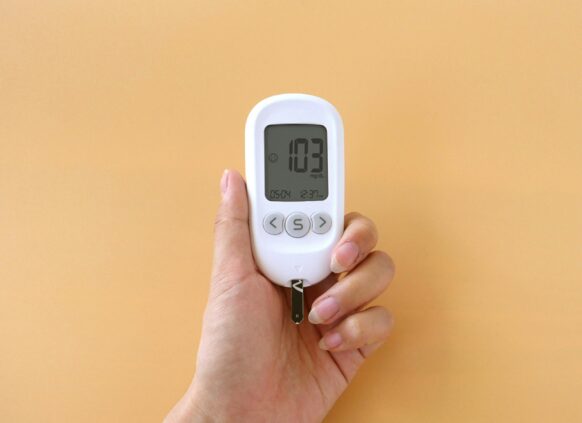 Hand holding a blood glucose meter displaying a reading of 103 mg/dL.