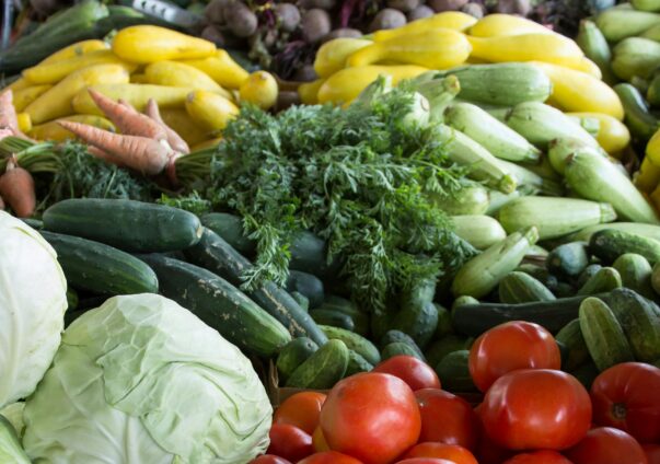 Fresh vegetables including tomatoes, cabbages, onions, cucumbers, squash, and carrots at a farmers market.