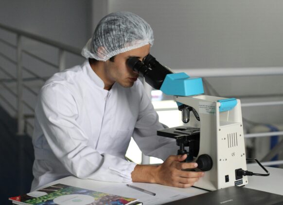 Scientist in a lab coat using a microscope for research and analysis.