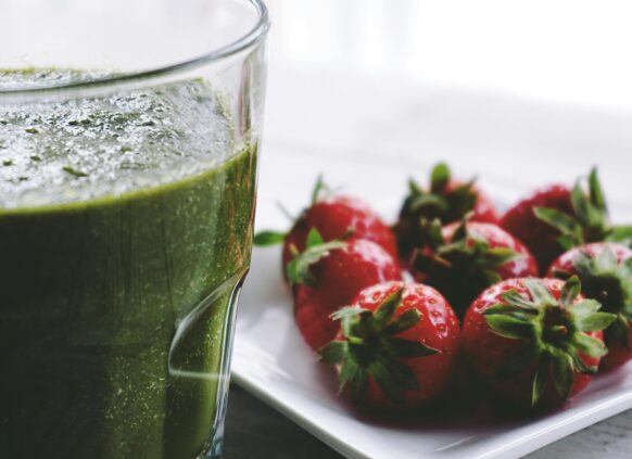 A healthy and green smoothie next to strawberries.