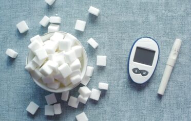 Blood glucose meter, lancet device, and sugar cubes symbolizing insulin resistance and diabetes risk.