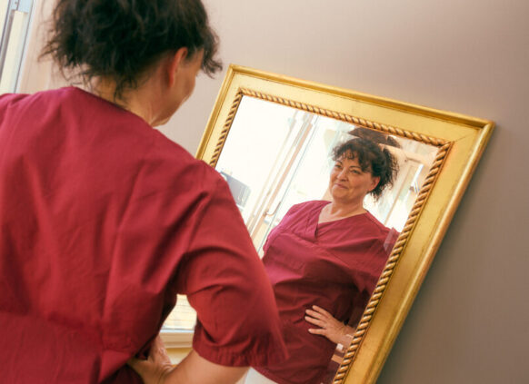 Woman in red top looking at herself confidently in a mirror.