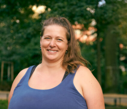 Smiling woman in a blue tank top standing outdoors in a park.