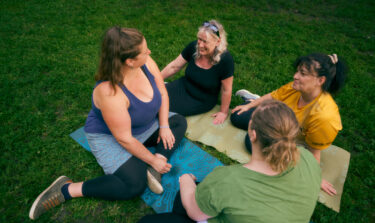 Group of women sitting on yoga mats in a park, smiling and talking.