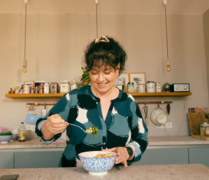 Woman smiling while eating a healthy meal in a modern kitchen.