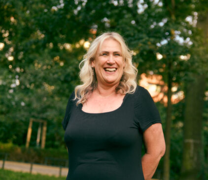 Smiling woman in a black dress standing outdoors in a green park.