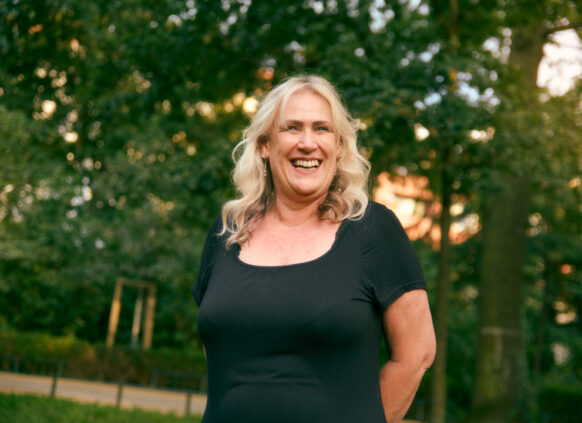 Smiling woman in a black dress standing outdoors in a green park.