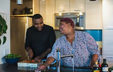 Couple enjoying time together in the kitchen while preparing food and cleaning.