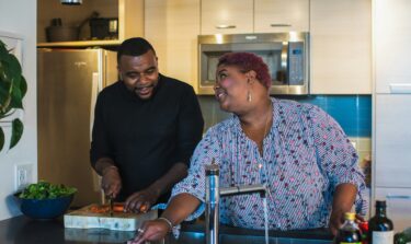 Couple enjoying time together in the kitchen while preparing food and cleaning.