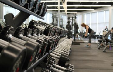 Dumbbells on a rack in a modern gym with a woman exercising in the background.
