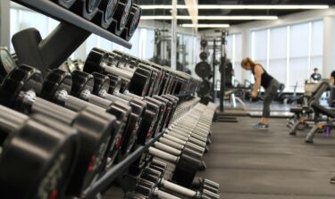 Dumbbells on a rack in a modern gym with a woman exercising in the background.