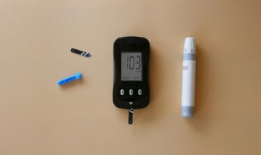 Blood glucose monitor with test strips, lancet, and lancing device on beige background.