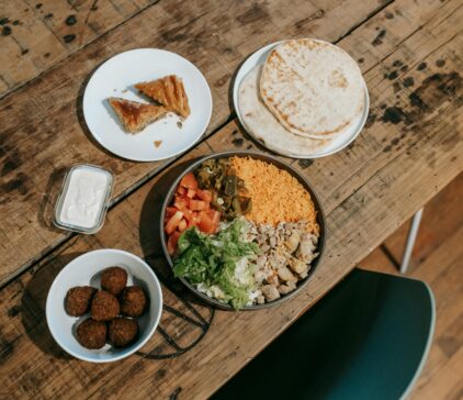 Mediterranean-style meal with rice bowl, falafel, pita bread, dessert, and dipping sauce on a wooden table.