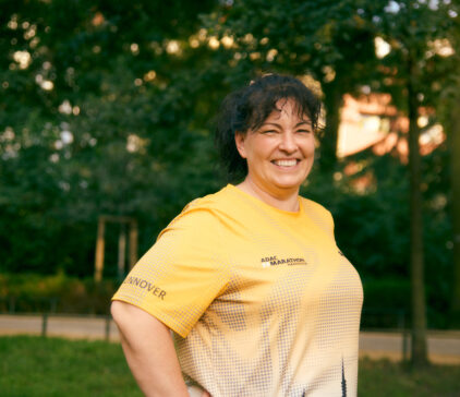 Smiling woman in a yellow marathon shirt standing outdoors in a park.