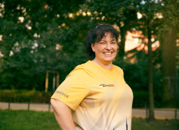 Smiling woman in a yellow marathon shirt standing outdoors in a park.