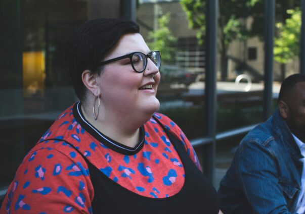 Plus-size woman smiling while talking outdoors with a friend, wearing hoop earrings and glasses.