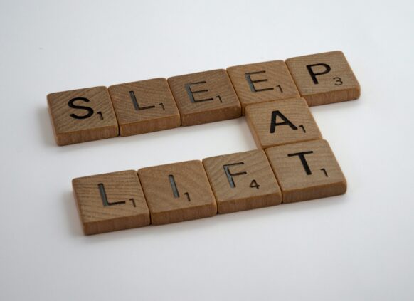 Wooden letter tiles arranged to spell “SLEEP,” “EAT,” and “LIFT” in a crossword pattern on a white background