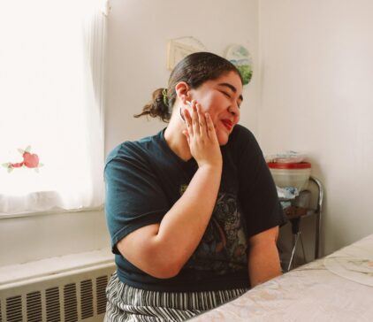 Happy woman sitting at a table, smiling with her hand on her cheek in a cozy home setting.